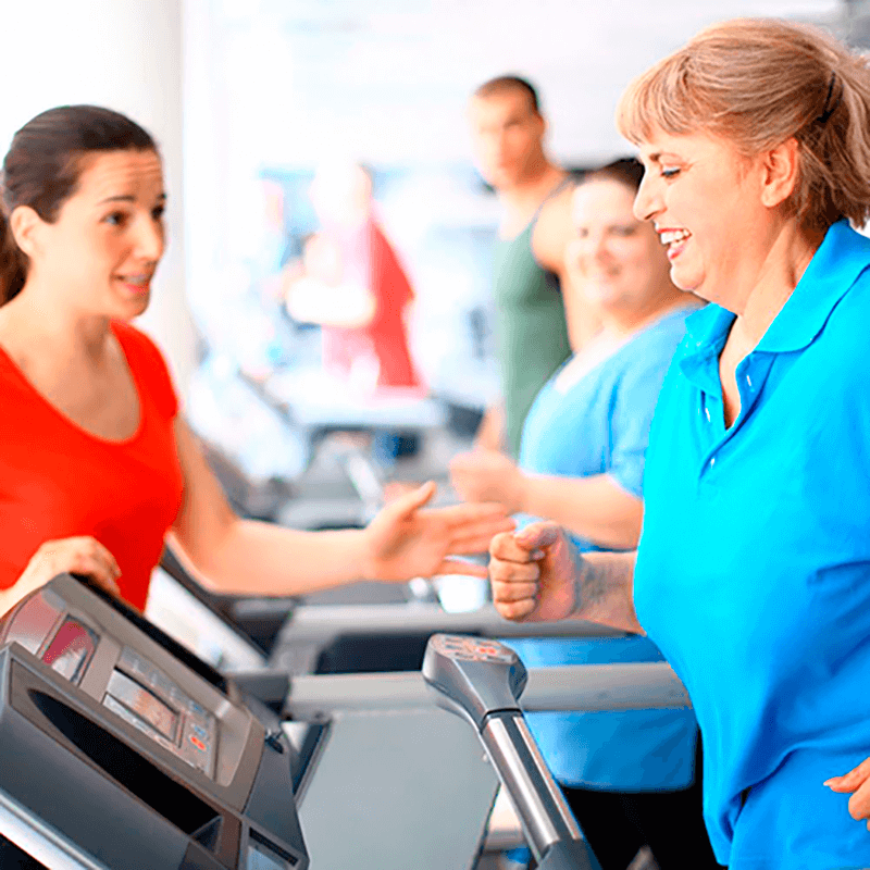 Woman smiling on treadmill with a trainer overseeing